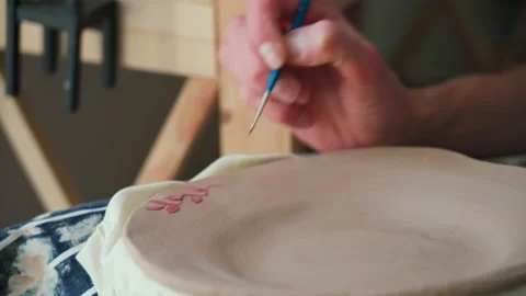 A potter's hands paint a ceramic plate with a brush. Close up Vidéo 234849626