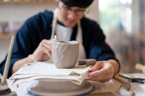 Pottery artist using tool adding texture to clay mug on a wheel at working .. Photos
