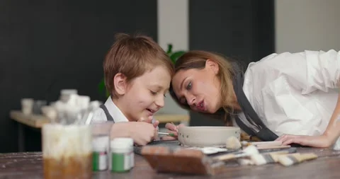 Pottery class workshop. Mother teaches her happy son drawing on clay bowl in Stock Footage 155992797
