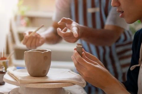 Pottery teacher explaining how to put a handle on clay mug at working table.. Photos