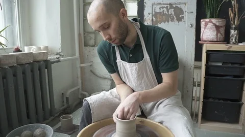 In pottery workshop man quickly makes high mug with hands on potter's wheel. Stock Footage 90130742