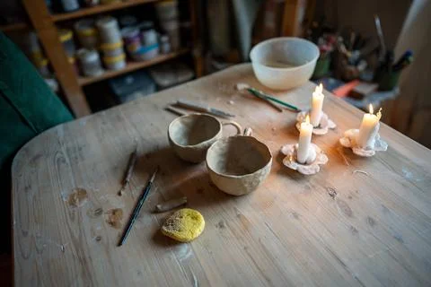 Pottery workshop wooden table featuring candles, clay tools, sponge and whi.. Stock Photos