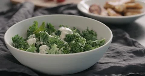 Pour caesar dressing on kale leaves in white bowl Stock Photos