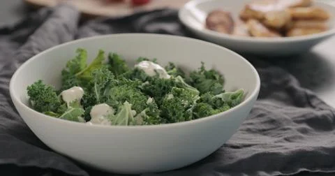 Pour caesar dressing on kale leaves in white bowl Stock Photos