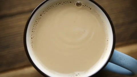 Pour cane sugar from spoon into cup of coffee with milk Stock Footage 106145515