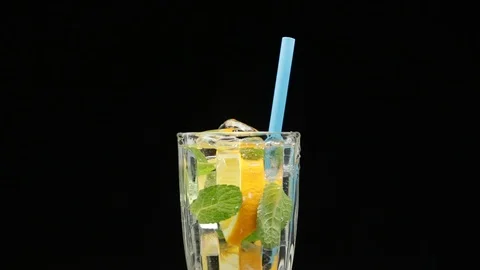 Pour a cold drink with mint, citrus and ice into a glass. on a black background. Stock Footage 116106627