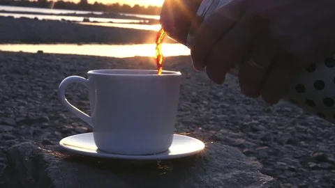 Pour a delicious hot tea or coffee by the river at sunset into a white cup from Stock Footage 80987174