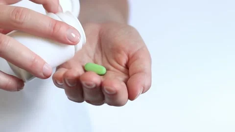 Pour the green tablets from the white bottle into your hand. Vitamins Stock Footage 247447330