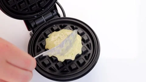 Pour the liquid waffle batter into a round, miniature waffle iron. Stock Footage 294564480
