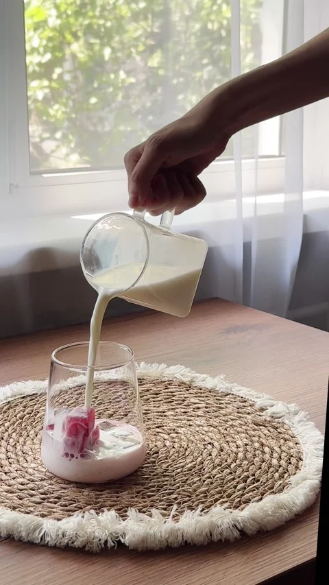Pour milk over cherry juice ice cubes in a clear glass Video stock 341134040