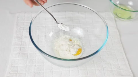 Pour a teaspoon of baking powder into a transparent bowl with eggs to prepare Stock Footage 231695802