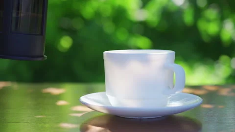 Pouring black coffee into a mug on a table in a garden landscape Stock Footage 223693844