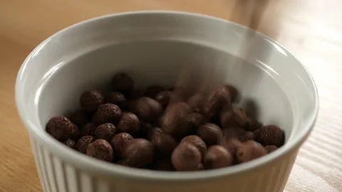 Pouring brown chocolate choco cereal balls into an empty white bowl Stock Footage 294696282