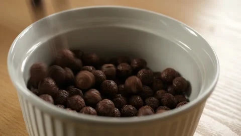 Pouring brown chocolate choco cereal balls into an empty white bowl Stock Footage 294696287