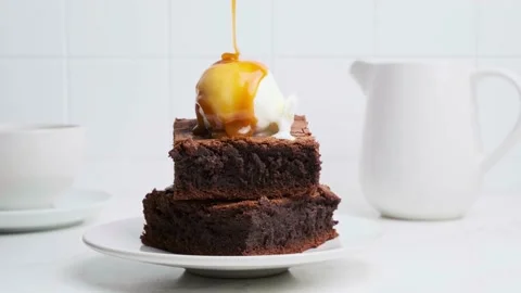 Pouring caramel on stack of brownie squares with scoop of ice cream Stock Footage 166528429