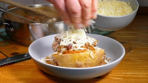 Pouring chilli con carne over a baked potato then adding grated cheese. Stock Footage 105748030