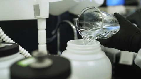 Pouring a clear liquid from a large graduated cylinder into a white bucket Stock Footage 127532645