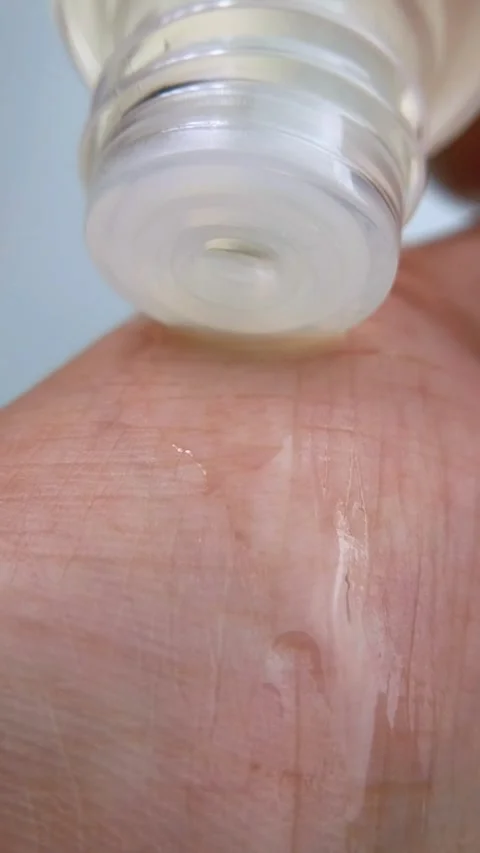 Pouring clear liquid from transparent product packaging onto hand skin. Stock Footage 334874576