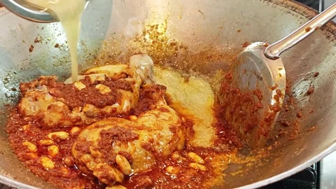 Pouring coconut milk over chicken Massaman curry paste in a wok. Vidéo 344560495