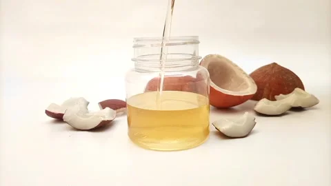 Pouring coconut oil in a jar with split coconuts and some coconut pieces Stock Footage 275670687