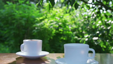 Pouring coffee into two cups on a table in a garden landscape Stock Footage 202644230