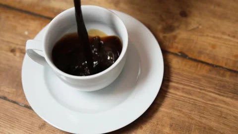 Pouring coffee into a white coffee cup on a wood table/ close up Stock Footage