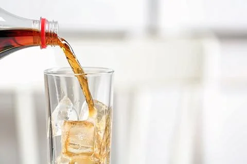 Pouring cola from bottle into glass on blurred background, closeup. Space for Stock Photos