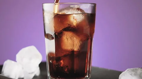 Pouring cola with ice cubes and bubbles in glass, slow motion. Stock Footage 92322933