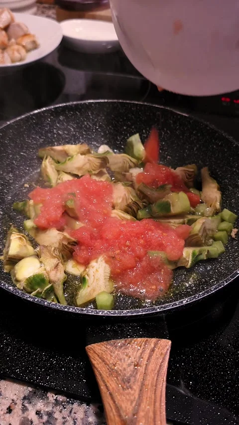 Pouring crushed tomatoes on artichokes while frying in olive oil in pan. Stock Footage 344967563