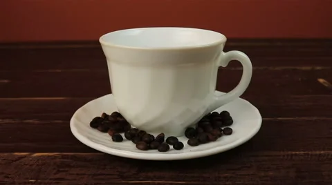 Pouring a cup of coffee with coffee beans on plate over brown wooden table Stock Footage 65284196