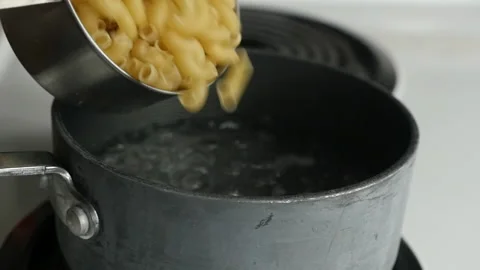 Pouring a cup of pasta into a boiling pot while cooking a meal Stock Footage 221177136