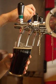Pouring dark craft beer from draft tap into pint glass at pub Photos