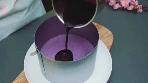 Pouring dark liquid onto purple mousse dessert in kitchen Видео 342883902
