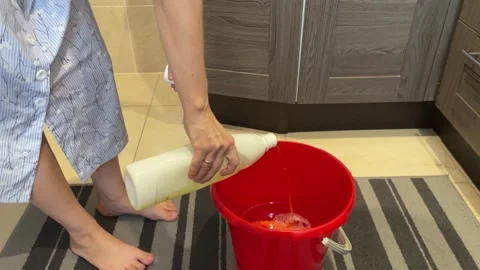 Pouring detergent onto orange mop inside red bucket on kitchen floor 库存影片 348240598