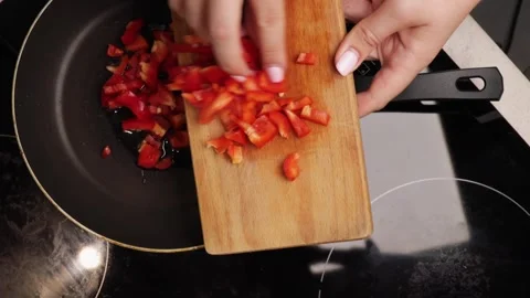 Pouring diced red bell pepper from wooden board into hot pan with oil for frying Stock Footage 317106930