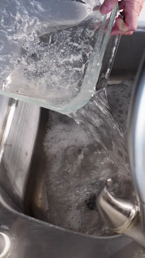 Pouring dirty baking dish water into kitchen sink slow motion vertical video Stock Footage 289923926