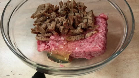 POuring eggs into minced meat and diced bread in a bowl and mixing ingredients Stock Footage 272995003