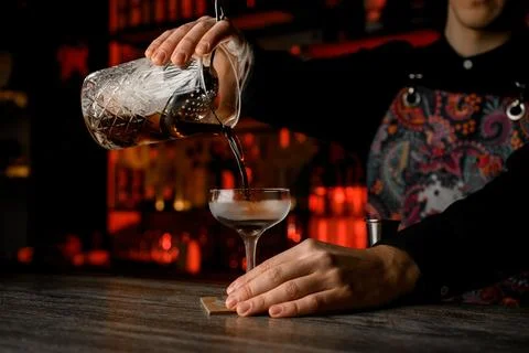 Pouring Elegance. Bartender skillfully pours a cocktail into a chilled glass. 스톡 사진