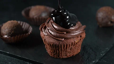 Pouring extra dark melted chocolate sauce over over a delicious, tasty cupcake Stock Footage 155552512