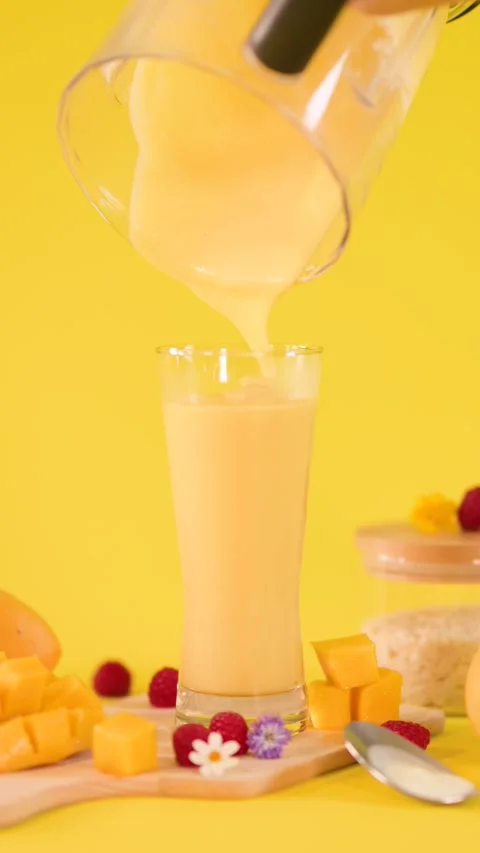 Pouring Fresh Mango Smoothie Into Tall Glass on Yellow Stock Footage 324027199