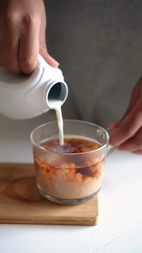 Pouring fresh milk into hot tea in glass mug Stock-Footage 331772452
