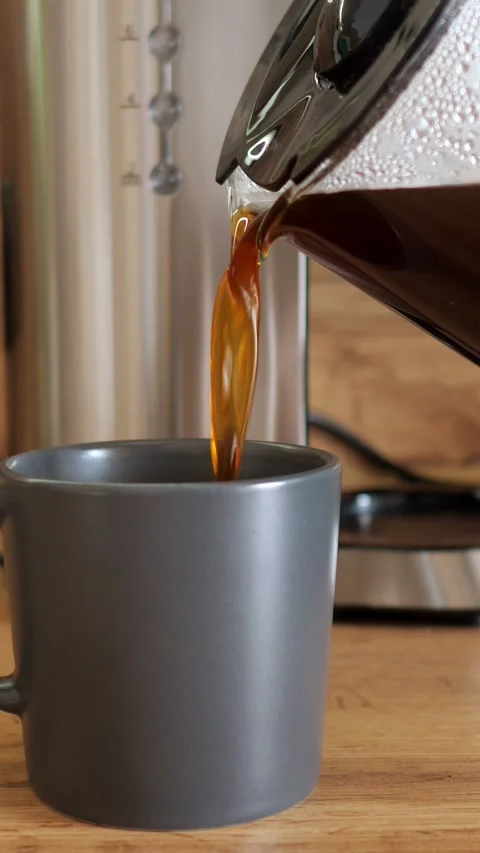 Pouring freshly brewed black coffee from a glass pot into a grey mug in the Stock Footage 341283043