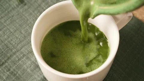Pouring freshly prepared green matcha tea from bowl into white ceramic cup... Stock Footage 345166364