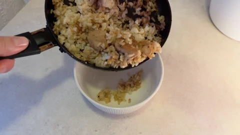 Pouring fried rice with meat into ceramic bowl on kitchen table. POV view of Stock Footage 280932717
