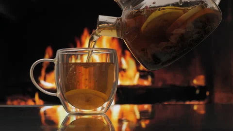 Pouring fruit tea in cup against background of a fireplace with a flame Stock Footage 263765300