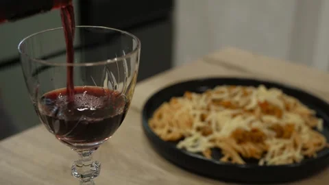 Pouring a glass of Red Wine while Pasta sits elegantly on the Table Stock Footage 311549166