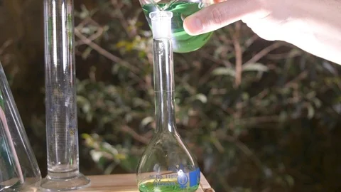 Pouring green liquid into a test tube in an outdoor environment with a pan Stock Footage 106938654