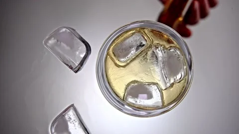 Pouring hard liqueur inside drinking glass over ice cubes Stock Footage 169247554