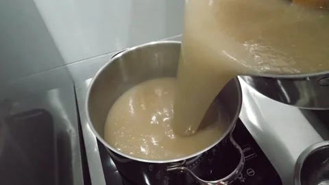 Pouring Homemade Bone Broth into Stainless Steel Pot on Induction Cooktop Stock Footage 345291939