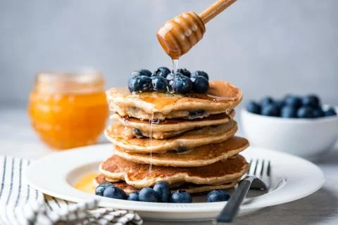 Pouring honey on stack of oat pancakes Stock Photos